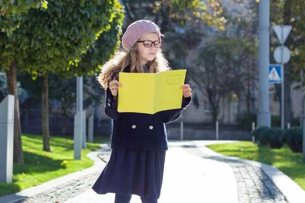 Οδός πορτρέτο του ένα χαριτωμένο κορίτσι με τα γυαλιά, παλτό, γαλλική μπερέ με ένα σημειωματάριο στα χέρια — Φωτογραφία Αρχείου