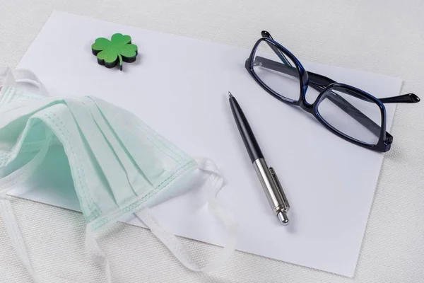 Papel limpo, uma folha de trevo verde e uma máscara protetora . — Fotografia de Stock