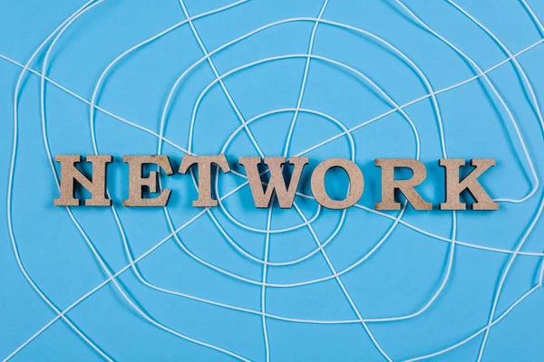 The word network with wooden letters in the form of an abstract spider web, blue background
