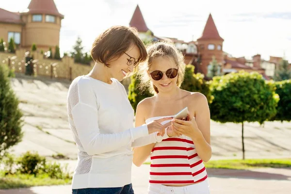 Moeder en tiener dochter portret. Achtergrond zomer stad, moeder en dochter op zoek bent in smartphone — Stockfoto