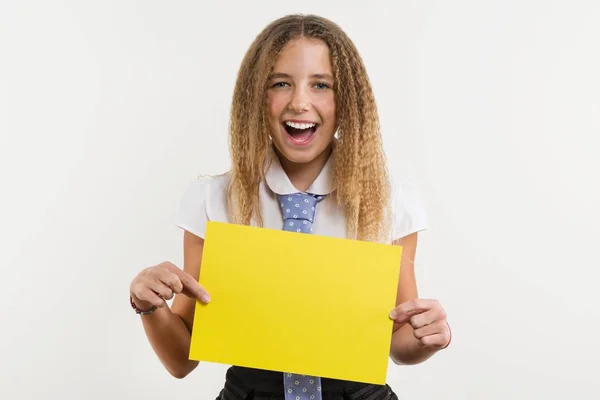 A smiling high school student, blonde with curly hair, holds a blank paper of yellow color, on which can be your promotional information. — Stock Photo, Image