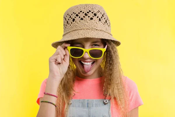 ช่วงฤดูร้อน เด็กสาววัยรุ่นในหมวกฟางและแว่นตากันแดด ตาข้างหนึ่ง แสดงภาษาบนพื้นหลังสีเหลือง — ภาพถ่ายสต็อก
