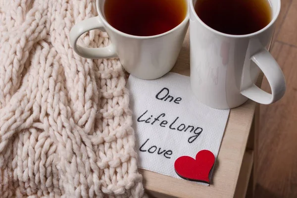 One long life of love is an abstract symbolic image. Couple of cups, background warm scarf, in home interior, napkin with text — Stock Photo, Image