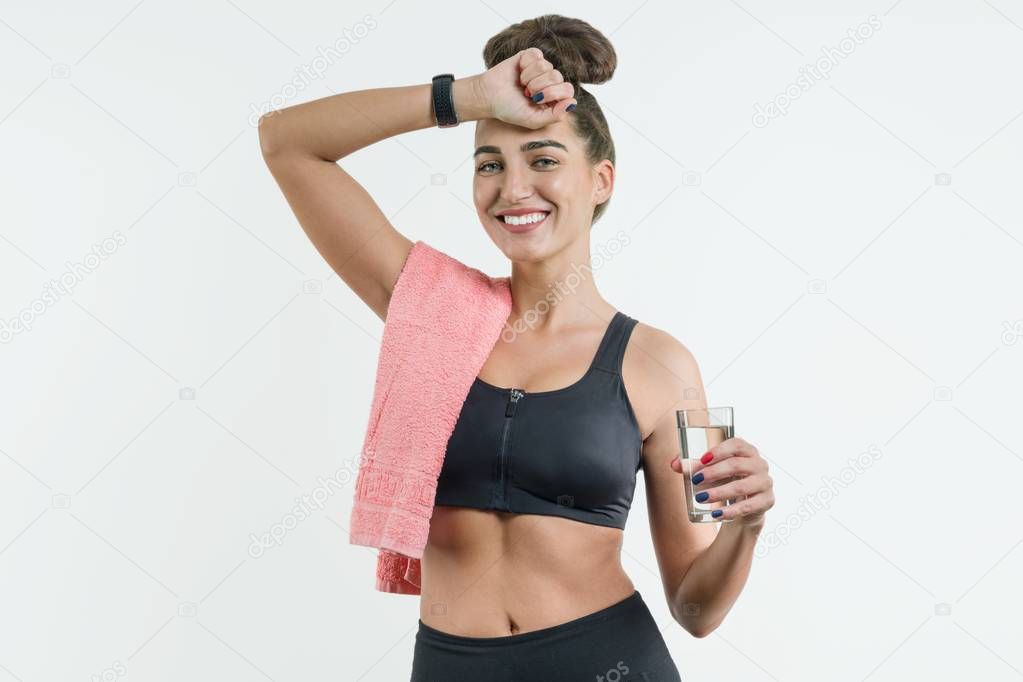 Positive smiling fitness woman drinking water against a white ba