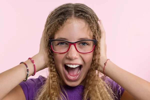 Chica adolescente con gafas, con el pelo largo se rasca la cabeza y es emocional desconcertado. Fondo de estudio rosa . — Foto de Stock