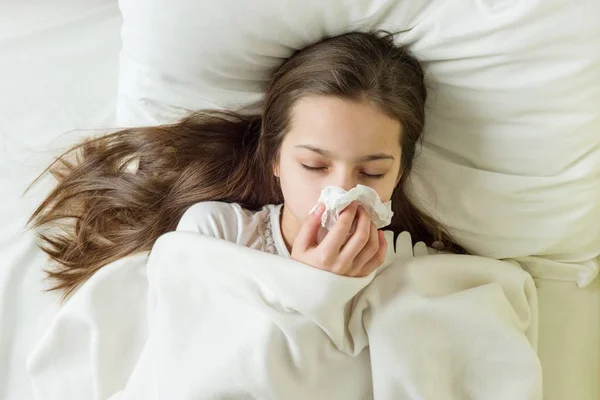 Enfermo chica en cama estornudando en pañuelo en el dormitorio —  Fotos de Stock