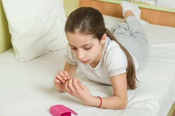 Девушке 10 лет дома на кровати в ее домашней одежде, ногти ее ногти с помощью маникюра аксессуары — стоковое фото