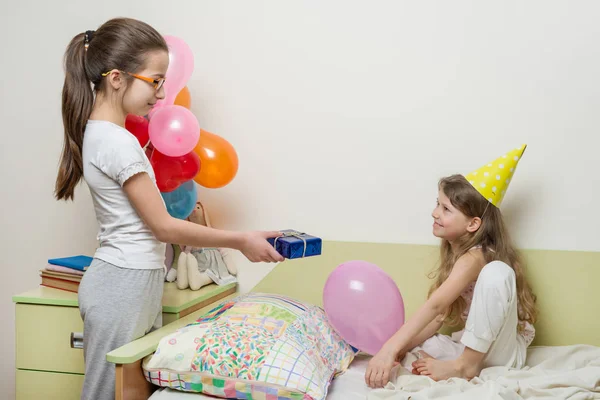 Geburtstag. ältere Schwester gibt Überraschungsgeschenk an ihre süße kleine Schwester. Kinder zu Hause im Bett — Stockfoto