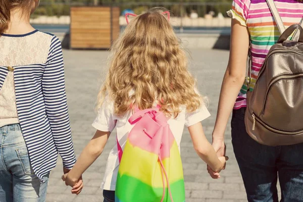 Вид сзади на детей трех девочек. Они держатся за руки, гуляют по городу . — стоковое фото