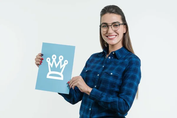 Positive young woman showing a crown sign on blue paper. White studio background — Stock Photo, Image