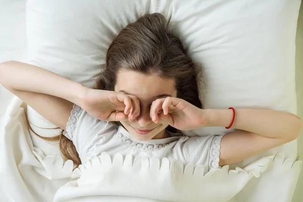 Girl child wakes up, rubs eyes. Lying on a pillow in bed, top view — Stock Photo, Image