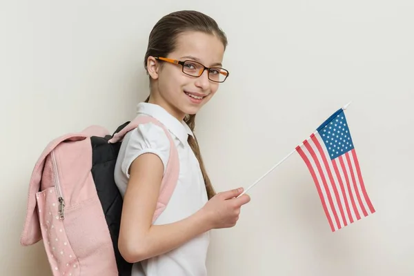 School child with a backpack holds the US flag, background bright wall in the school — Stock Photo, Image