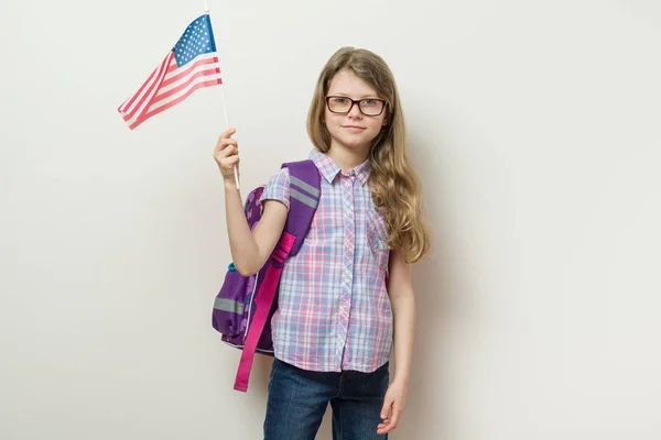 เด็กนักเรียนที่มีกระเป๋าเป้สะพายหลังถือธงสหรัฐอเมริกาผนังเบื้องหลังที่สดใสในโรงเรียน — ภาพถ่ายสต็อก