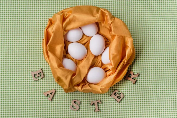 White eggs in an abstract nest of yellow textures, green background of tablecloths in the kitchen — Stock Photo, Image