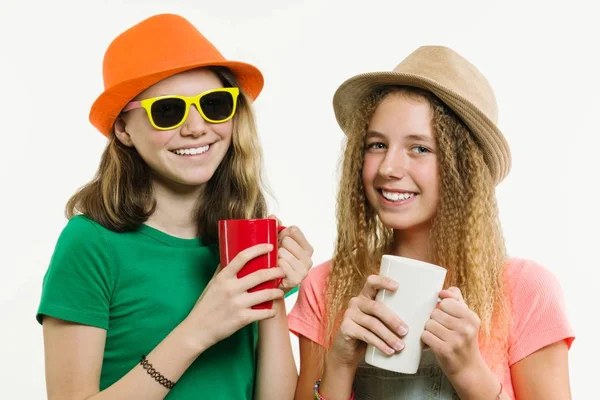 Filles copines 12-14 ans, sur un fond blanc dans des chapeaux parler, tenant des tasses — Photo