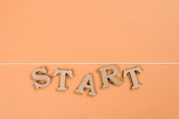 Palabra comenzar con letras de madera y comenzar la línea sobre un fondo naranja — Foto de Stock