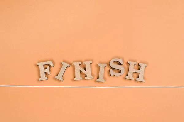 Palavra de acabamento com letras de madeira e linha de chegada em um fundo laranja — Fotografia de Stock