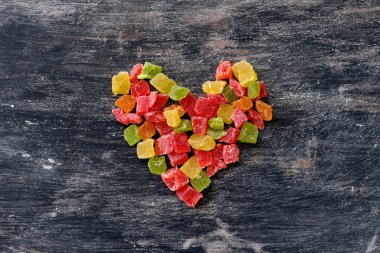 Koyu ahşap antika arka plan üzerinde kalp şeklinde çok renkli meyve şekerlenmiş.