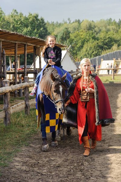 Kyiv region, UA, 24-09-2011, The child sits on a horse, costumed woman helps. Costume Recreation Park Kyivan Rus of medieval period Kyiv Rus.