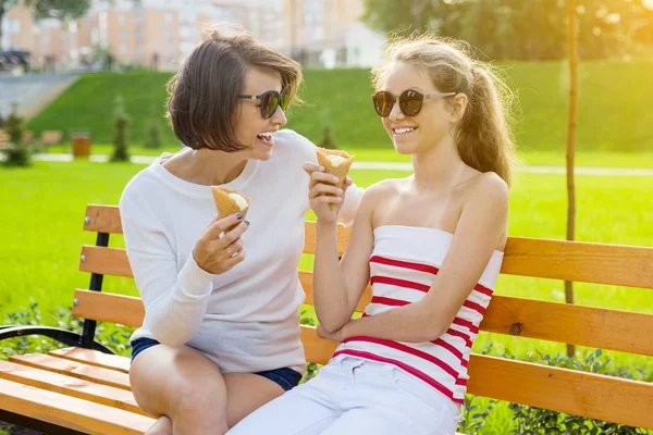 Vacaciones con la familia. Feliz joven madre y linda hija adolescente en el parque de la ciudad comiendo helado, hablando y riendo — Foto de Stock