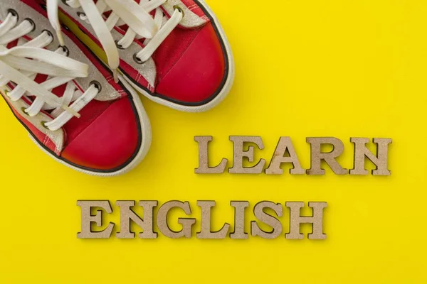 Вивчати англійську мову, слова з дерев'яними листи з жовтому тлі перед червоний молоді кросівки — стокове фото