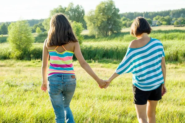 Мать и дочь-подросток держатся за руки, вид сзади. Фотография на природе в солнечный летний день . — стоковое фото