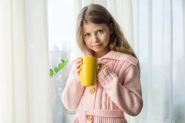 เด็กผู้หญิง อายุ 7 ขวบ ผมบลอนด์ ผมยาวคลื่นในเสื้อกันหนาวถักอบอุ่นถือถ้วยชา — ภาพถ่ายสต็อก