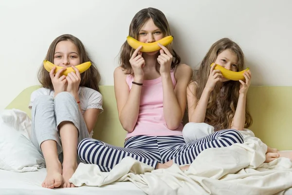 Systrar av barn i pyjamas spelar på morgonen i sängen. Använda bananer för smiley snark — Stockfoto