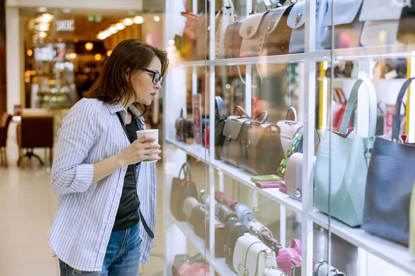 Взрослая женщина смотрит на витрину с сумками и аксессуарами в торговом центре — стоковое фото