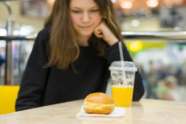 Дівчинка-підліток в кафе їсть торт і апельсиновий сік. Фокус на торті, фоновому торговому центрі розважального центру — стокове фото