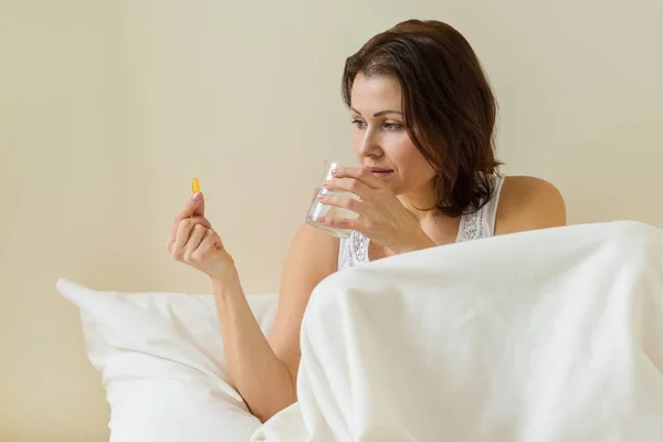 Vrouw neemt pil met omega-3 en een glas vers water in bed ochtend houden. Vitamine D, E, een vis olie capsules. — Stockfoto