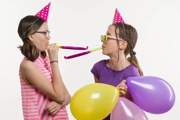 Ragazze adolescenti a una festa. Ragazze su uno sfondo bianco, in cappelli festivi, che soffiano nei tubi . — Foto Stock