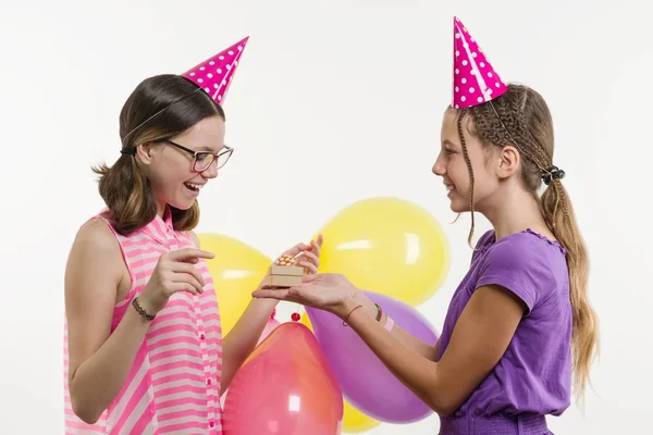 Вечірка на день народження. Дівчата-підлітки дарують подарунок. Білий фон, у святкових капелюхах з повітряними кульками . — стокове фото