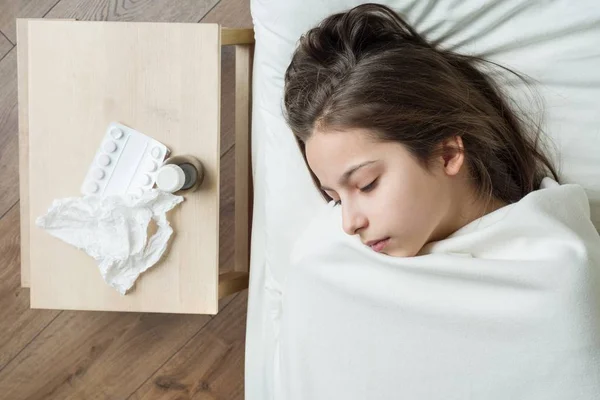 Koude griepseizoen. Ziek meisje kind in bed, in de buurt van bed medicatie servet — Stockfoto