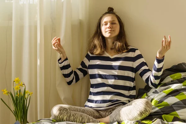 Nastoletni Dziewczyna medytuje i uśmiechając się siedząc w Joga pozuje na łóżku — Zdjęcie stockowe