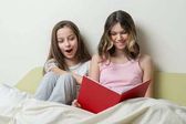 A pizsama két tizenéves lány az ágyban otthon ülni, és nézni a könyvet.