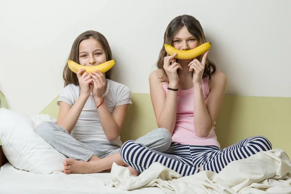 Sestry děti v pyžamu hrát do rána v posteli. Pro snark smajlík použít banány — Stock fotografie