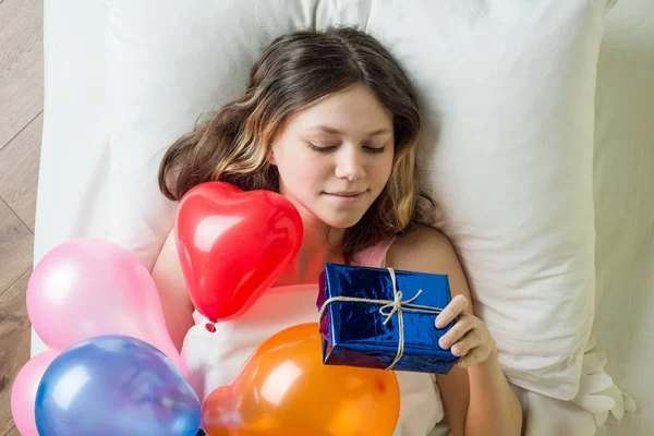 Narozeninový den. Dospívající dívka ležela v posteli na polštáři drží dárek, pohled shora — Stock fotografie