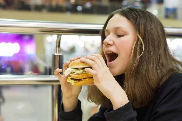 먹는 햄버거, 배경 쇼핑몰 엔터테인먼트 센터 십 대 소녀 — 스톡 사진