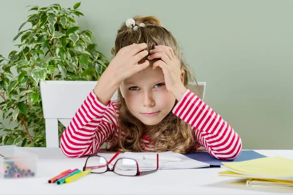 Niña se ríe, se sienta en un escritorio, dibuja y escribe, las manos con la cabeza . — Foto de Stock