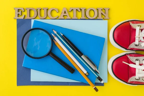 O conceito de educação. Tênis vermelhos, material escolar, livros, cadernos com fundo amarelo — Fotografia de Stock