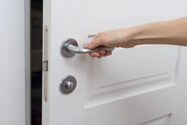 Handen öppnar dörren något. Detalj av en vit innerdörr med en chrome dörrhandtag och spärr — Stockfoto