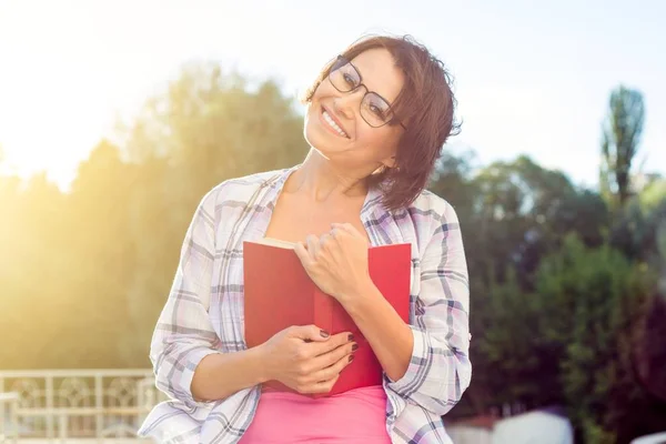 Smiling beautiful brunette relaxing outdoors and reading book. Urban style background — Stock Photo, Image