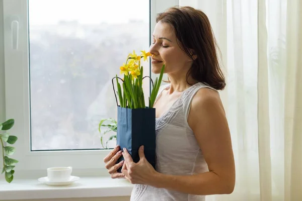 Mujer madura sosteniendo ramo de flores amarillas de primavera, disfruta de las flores . — Foto de Stock