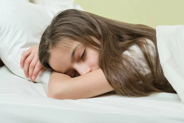 Девочка с длинными каштановыми волосами спит на подушке в постели — стоковое фото