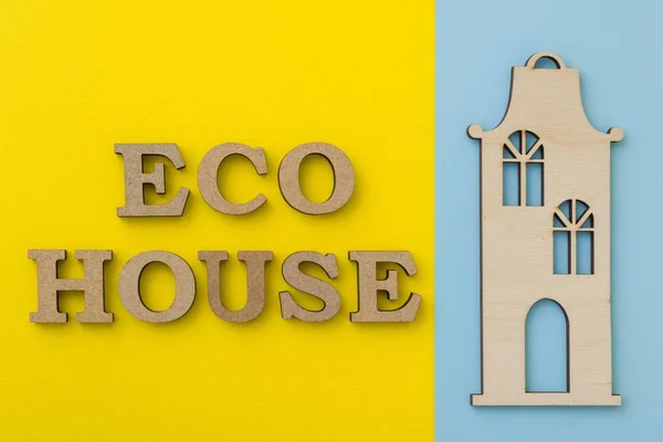 Koncepcja oprawy eco. Dom eko słowo, żółtym, niebieskim tle, drewniany model domu — Zdjęcie stockowe