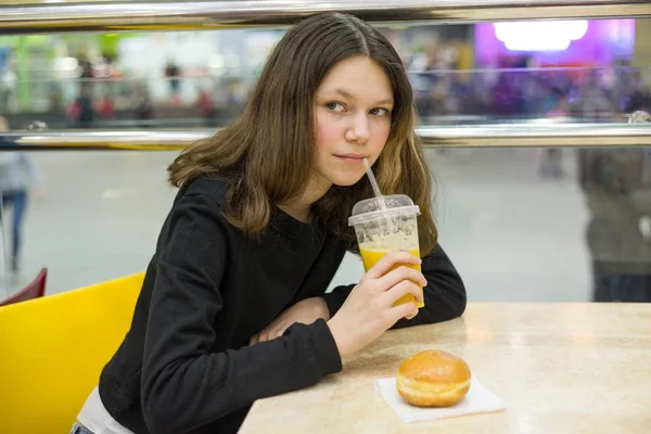 Dospívající dívka v kavárně jíst koláče a pomerančový džus, pozadí nákupní centrum zábavní centrum — Stock fotografie