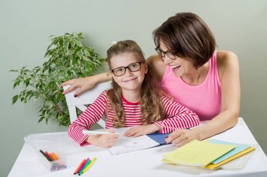 Anne ve küçük kızı masada birlikte evde not defterinde yazmak.