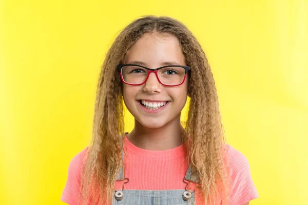 Una adolescente con gafas mira a la cámara y sonríe, fondo amarillo del estudio . —  Fotos de Stock