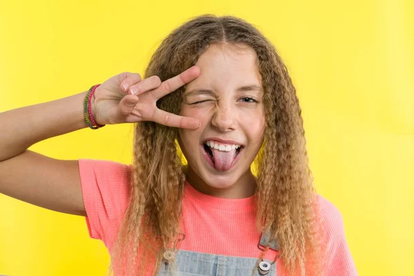 Menina adolescente feliz gesticulando, mostrando a língua, cobrindo um olho, fundo de estúdio amarelo brilhante — Fotografia de Stock